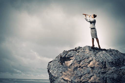 Woman on a coastal rock looking through a looking glass